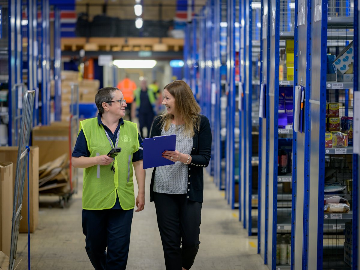Two team members walking through a warehouse aisle with a checklist